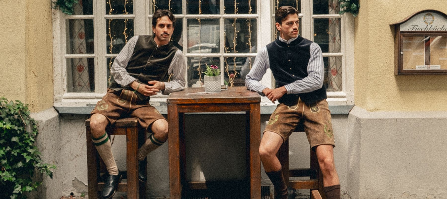 Lederhose braun, Trachtenhemd, Trachtenweste & Kniestrümpfe - zwei Männer vor Fassade